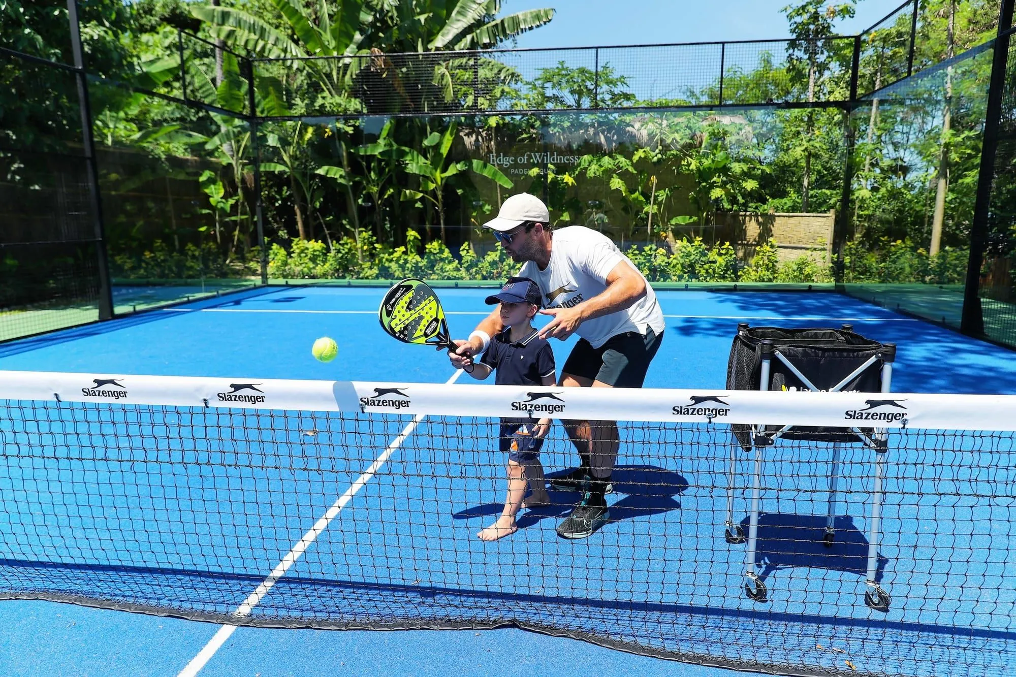 Entrenador guiando a un niño en una pista de pádel