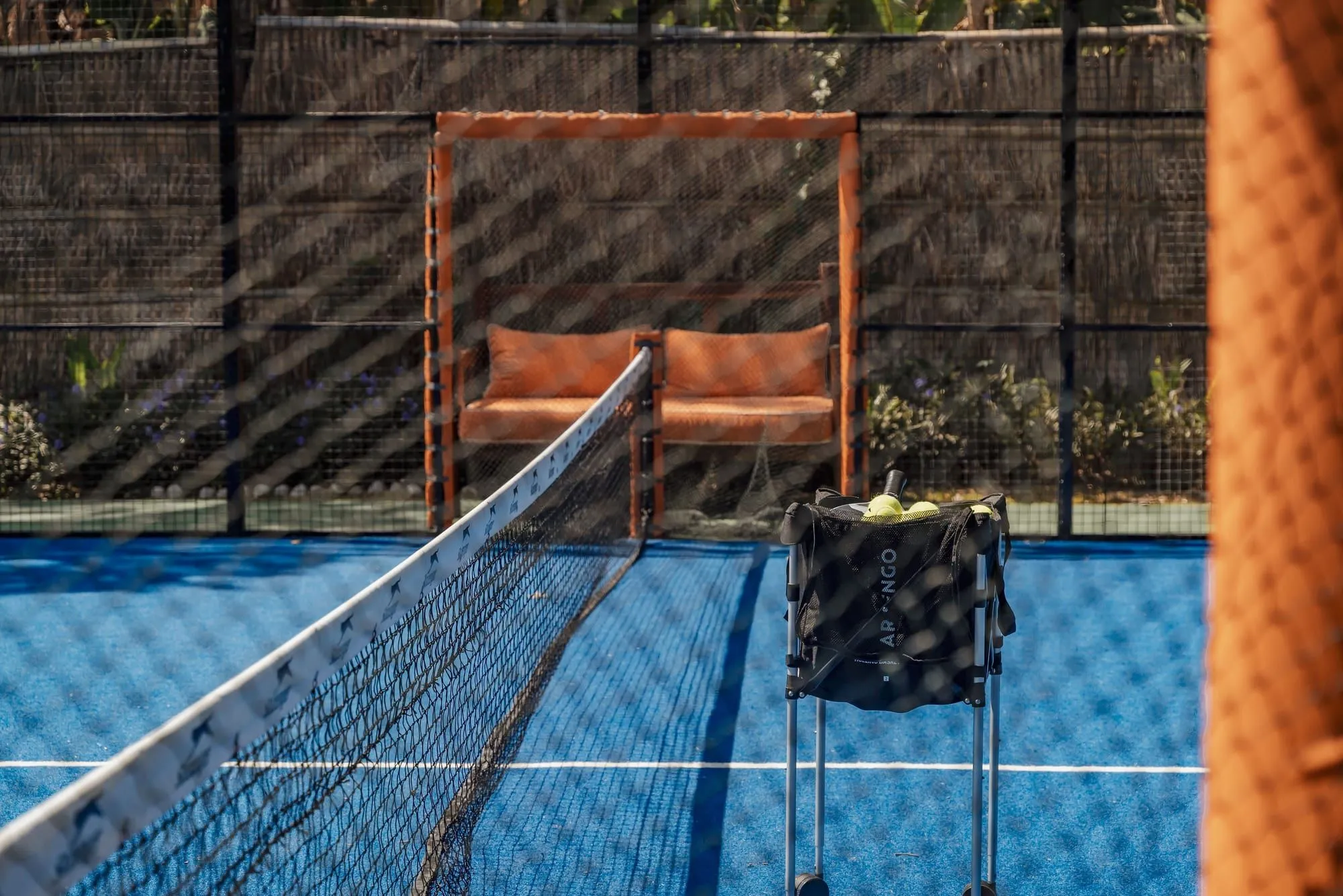 Padel court with a ball hopper and orange seating