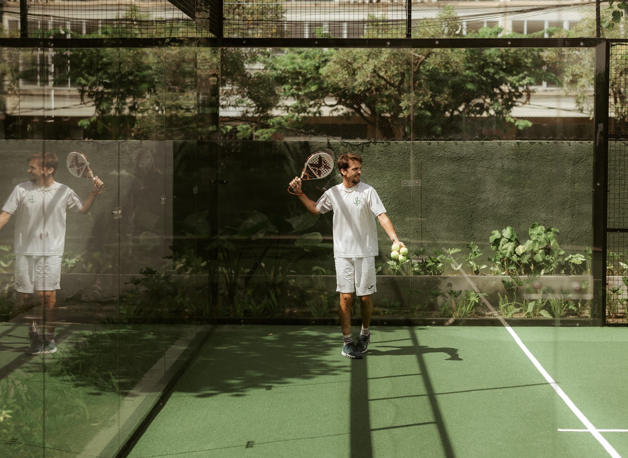 Padel coach standing on court with a racket and balls